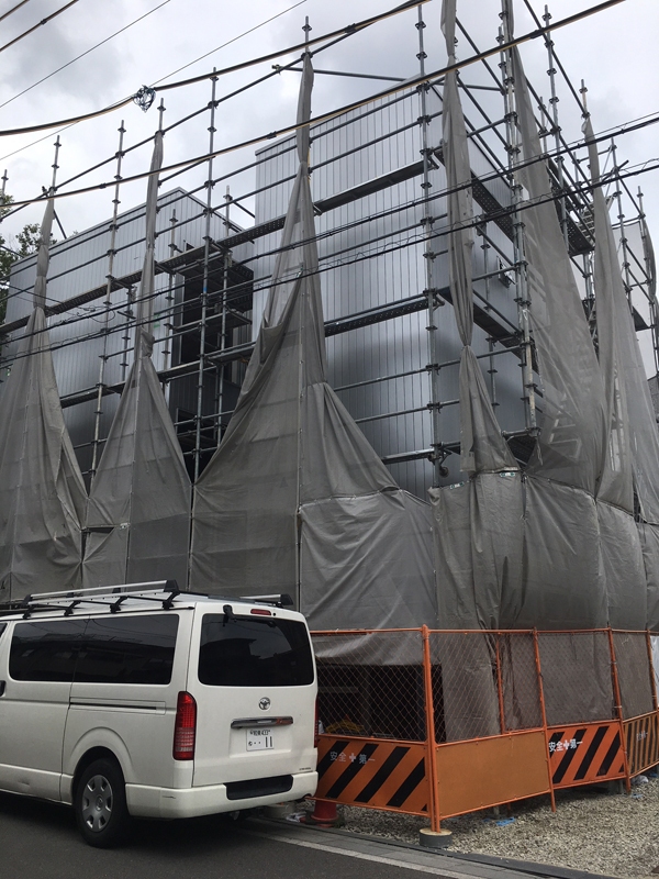 高槻のオフィス：足場と養生シートの間から銀色の金属外壁が見える施工中の外観