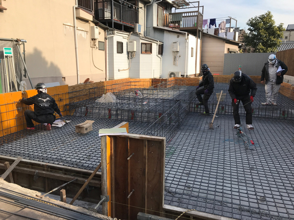 海老江の家：型枠内に格子状の鉄筋を組み、基礎の配筋作業を進める職人たち